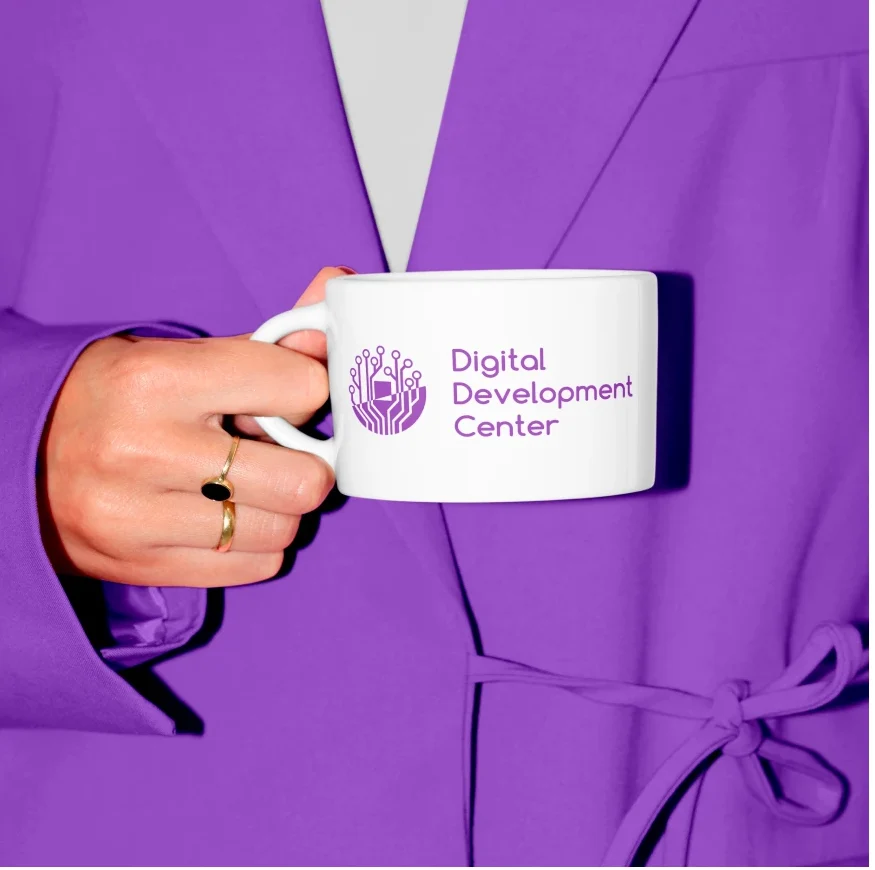 Weiße Tasse mit Logo, gehalten vor violettem Stoff